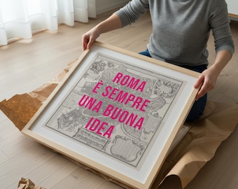 Può includere: Una stampa di mappa incorniciata con il testo "ROMA È SEMPRE UNA BUONA IDEA" in rosa acceso. La mappa è in bianco e nero, incorniciata in legno chiaro. La stampa è tenuta da una persona.