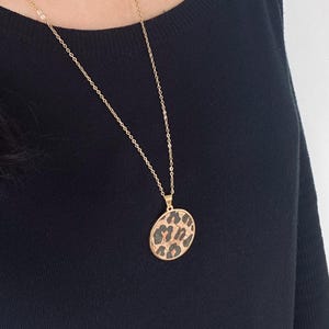 Könnte beinhalten: Eine goldene Kettenkette mit einem runden Anhänger mit Leopardenmuster.