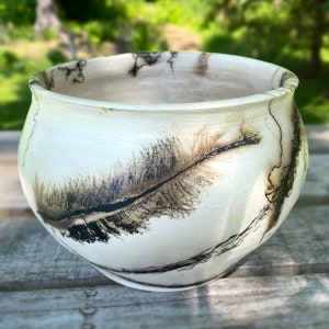 May include: White ceramic pot with black and brown feather-like designs. The pot has a rounded shape and a wide opening.