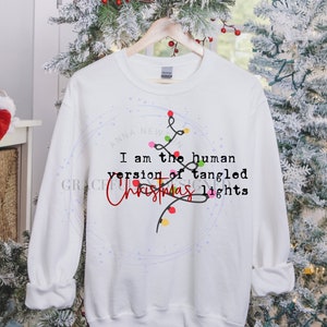 May include: White sweatshirt with a Christmas lights design and the text "I am the human version of tangled Christmas lights".