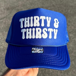 May include: A bright blue trucker hat featuring a foam front panel with the white text THIRTY & THIRSTY in a bold, wavy font. The cap includes a matching blue mesh back, a blue cord detail across the brim, and an Otto brand sticker on the front.