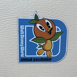 Pu&ograve; includere: Un magnete blu e bianco con un uccello arancione dei cartoni animati e il testo "Walt Disney World annual passholder".