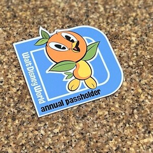 Pu&ograve; includere: Adesivo blu e arancione con un personaggio di cartone animato di un uccello arancione. L'adesivo dice "Walt Disney World annual passholder".