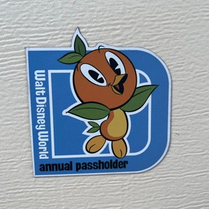 Pu&ograve; includere: Un magnete blu e bianco con il logo di Walt Disney World e le parole "annual passholder". Un uccello arancione dei cartoni animati con foglie verdi &egrave; al centro del magnete.