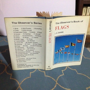 May include: A vintage book titled "The Observer's Book of Flags" by L.O. Evans. The book cover features a colorful illustration of various flags against a blue sky background. The book is part of a series, as indicated by the text "The Observer's Series" on the left side of the cover.