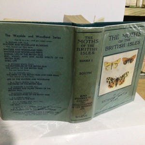 May include: A teal-coloured book from the Wayside and Woodland Series, titled "The Moths of the British Isles". The cover features moth illustrations. The spine indicates "Series 1" and "South".
