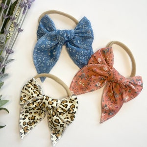 May include: Three fabric hair bows with elastic bands. The bows are in a blue floral print, a pink floral print, and a brown and white leopard print.