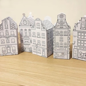 May include: Five black and white paper model houses with different details, including windows, doors, and roofs. The houses are arranged in a row on a wooden surface.