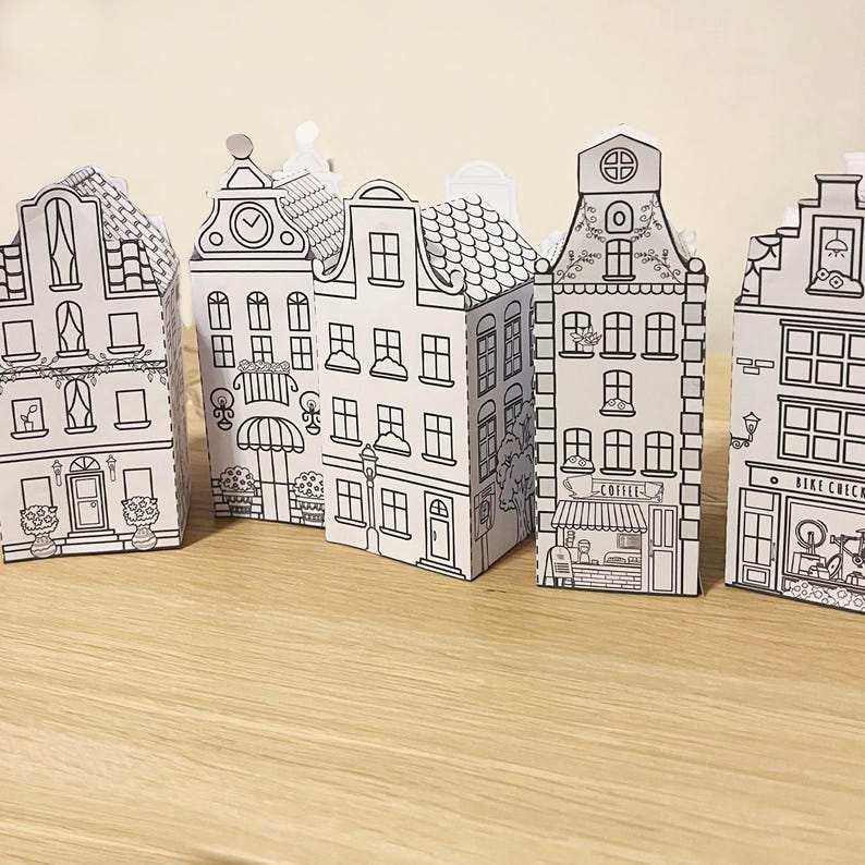 May include: Five black and white paper model houses with different details, including windows, doors, and roofs. The houses are arranged in a row on a wooden surface.