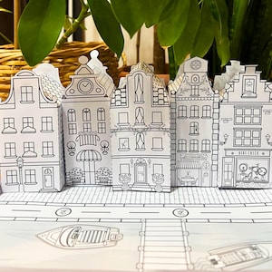 May include: Black and white printable papercraft model of a row of five European-style houses with a boat and a ladder in the foreground. The houses have details like windows, doors, and signs that say "Restaurant" and "Bike Check".