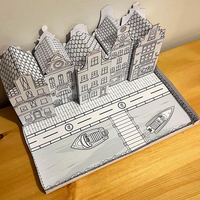 May include: A paper model of a Dutch village with houses, a canal, and boats. The model is made of white paper and is unpainted.