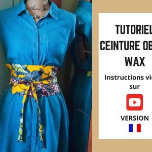 May include: A blue denim dress is cinched at the waist with a colorful Obi belt. The belt features a vibrant yellow and floral pattern. Text on the right side reads "TUTORIEL CEINTURE OBI EN WAX" and "Instructions vidéo sur" with a YouTube logo.