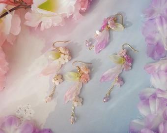 Puede incluir: Un par de aretes delicados con acentos florales rosas y verdes. Los aretes presentan una cadena colgante con pequeñas cuentas rosas y verdes. Los aretes son de metal y tienen un acabado dorado.