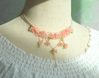 May include: A delicate gold necklace with pink flower accents. The necklace has a layered design with cascading flowers and a pendant.