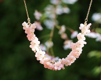 May include: A delicate gold chain necklace with pink flower-shaped beads. The necklace is made of small, delicate pink flowers that are strung together on a gold chain. The flowers are arranged in a cascading pattern, creating a beautiful and feminine look.