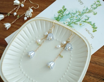 May include: A pair of delicate earrings with a floral design. The earrings feature small white flowers and pearls hanging from gold chains.