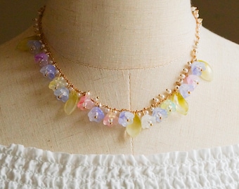 May include: A delicate necklace featuring a gold chain adorned with small, colorful flower charms in shades of pink, yellow, and blue. The necklace is displayed on a mannequin, showcasing its intricate design and pastel color palette.
