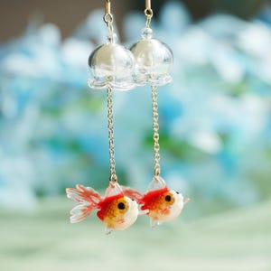 May include: Goldfish dangle earrings with clear glass bell charms and gold chains. The goldfish are red and white with black eyes.