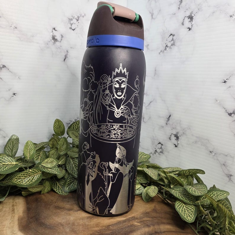 Puede incluir: Una botella de agua aislada azul oscuro con un dise&ntilde;o plateado grabado con villanos de Disney. La botella tiene una tapa negra con una banda azul y un asa marr&oacute;n. El dise&ntilde;o incluye im&aacute;genes de la Reina Malvada y otros personajes.