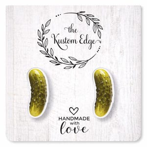 May include: Two pickle-shaped earrings on a white background with the text "the Kustom Edge" and "Handmade with love". The earrings are a bright green color with a yellow highlight.