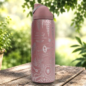 May include: A dusty rose water bottle with a silver-toned graphic print featuring a Lady's Gazette newspaper design, a bee, flowers, and the text "PERHAPS I AM more myself THAN I HAVE EVER BEEN." The bottle has a matching dusty rose lid with a gray handle.
