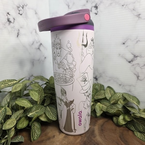 Puede incluir: Una botella de agua aislada Owala de color rosa claro con tapa y asa moradas. La botella presenta dibujos lineales en negro y plata de villanos de Disney. La botella es cil&iacute;ndrica y tiene una tapa abatible.