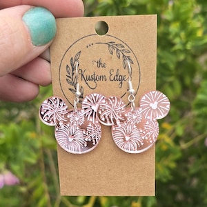 Puede incluir: Pendientes de oro rosa con un diseño de silueta de Mickey Mouse con motivos de fuegos artificiales blancos. Los pendientes están hechos por "The Kustom Edge".