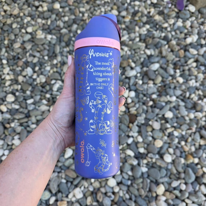 A person's hand holding a blue and pink water bottle with a textured surface in the background.