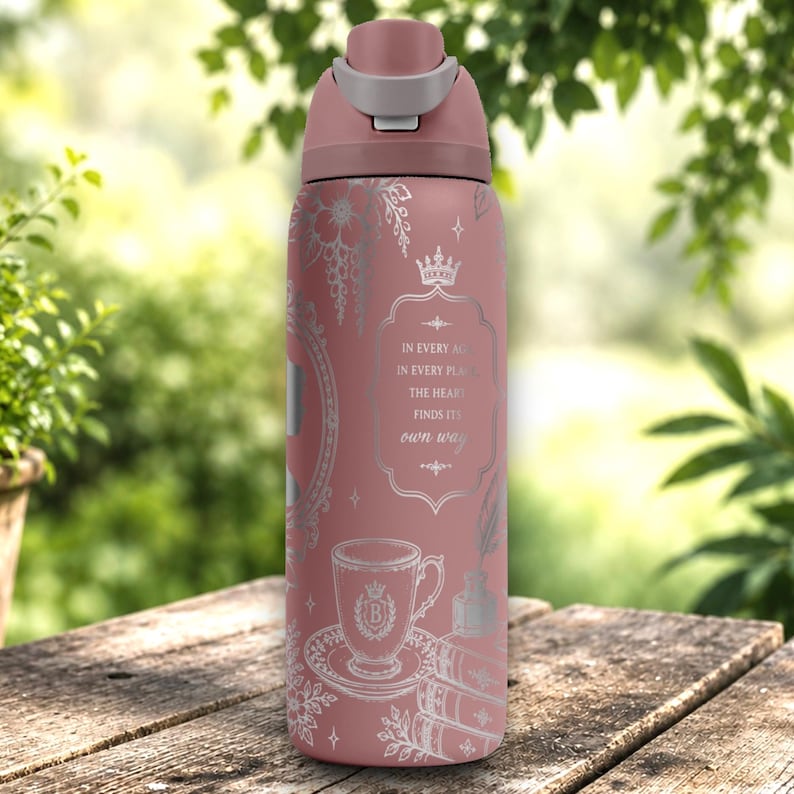 May include: A dusty rose water bottle with a silver-toned graphic print featuring a teacup, a stack of books, and a crown. The text reads: IN EVERY AGE IN EVERY PLACE THE HEART FINDS ITS own way. The bottle has a matching rose-colored lid with a gray accent.