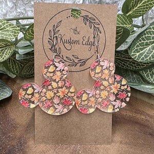May include: A pair of clear acrylic earrings in a Mickey Mouse shape, filled with autumn leaves in shades of red, orange, and yellow. The earrings hang from silver-colored hooks and are displayed on a brown card with the text "The Kustom Edge".