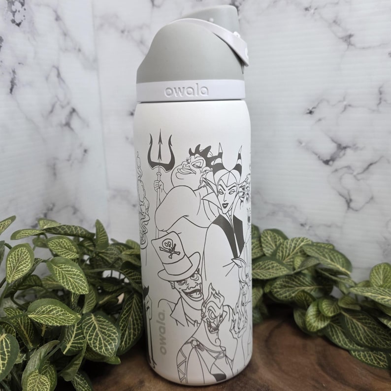 Puede incluir: Botella de agua Owala blanca con tapa gris, con una ilustraci&oacute;n en blanco y negro de villanos de dibujos animados. La botella tiene el nombre de la marca "owala" impreso. Rodeada de follaje verde.