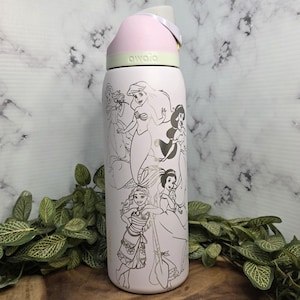 Pode incluir: Uma garrafa de &aacute;gua isolada rosa claro com tampa flip-top. A garrafa apresenta um design prateado de princesas da Disney. A tampa &eacute; rosa claro e cinza, com a marca "awala" impressa no topo.