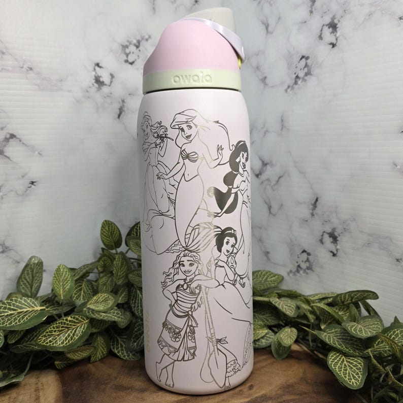 Pode incluir: Uma garrafa de &aacute;gua isolada rosa claro com tampa flip-top. A garrafa apresenta um design prateado de princesas da Disney. A tampa &eacute; rosa claro e cinza, com a marca "awala" impressa no topo.