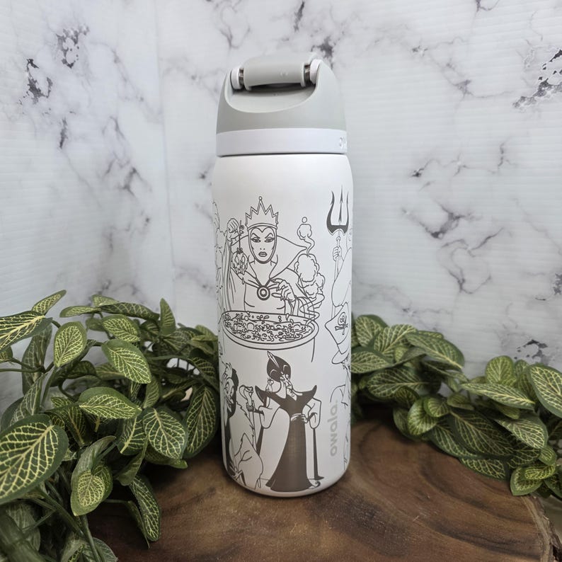 Puede incluir: Botella de agua aislada blanca con tapa gris e ilustraci&oacute;n en blanco y negro de villanos de Disney. La botella tiene una tapa abatible y un dise&ntilde;o que envuelve toda la botella. La botella est&aacute; sobre una superficie de madera.