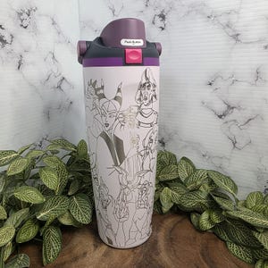 Puede incluir: Un termo de viaje de acero inoxidable con tapa morada y gris. El cuerpo rosa claro presenta un dibujo lineal en blanco y negro de varios villanos de dibujos animados. La tapa tiene un bot&oacute;n para abrir y cerrar.
