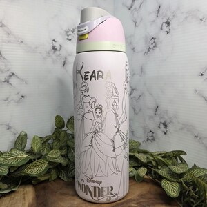 Pode incluir: Uma garrafa de &aacute;gua rosa claro com uma tampa cinza e rosa. A garrafa apresenta uma ilustra&ccedil;&atilde;o em preto e branco de princesas da Disney e o texto "Keara" e "Disney Wonder".