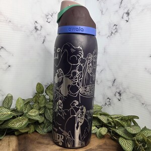 Puede incluir: Una botella de agua Owala azul oscuro con un dise&ntilde;o plateado grabado de villanos de Disney. La botella tiene una tapa marr&oacute;n, verde y azul. La palabra "owala" est&aacute; impresa en la banda azul.