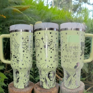 May include: Three light green travel mugs with silver lids and handles. Each mug features a design of Tinkerbell, stars, and the words "Believe" and "All you need is faith, trust, and a little bit of pixie dust."