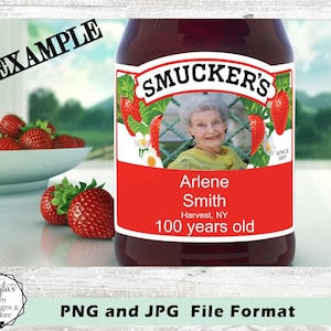 May include: A Smucker's jar label featuring a photograph of an elderly person, the text Arlene Smith, Harvest, NY, 100 years old, and Since 1897. The label includes red strawberry illustrations, green leaves, and white flowers on a white background.