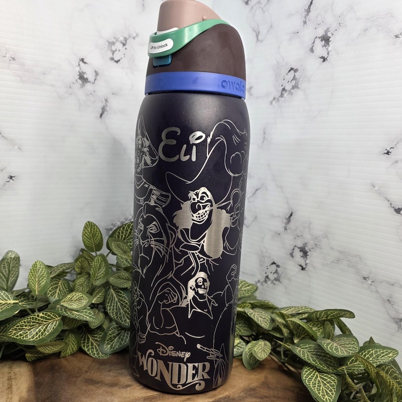 Puede incluir: Una botella de agua Owala azul oscuro con contornos plateados de villanos de Disney. La botella tiene una tapa marr&oacute;n y verde con el texto "Ultra Unlock". El texto "Eli" y "Disney Wonder" tambi&eacute;n son visibles.