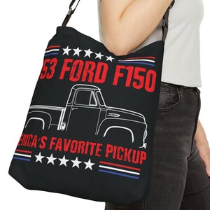 以下が含まれることがあります： 1953年製のフォードF150ピックアップトラックの白いシルエットが描かれた黒いトートバッグ。テキスト「'53 Ford F150」は赤色、「America's Favorite Pickup」は白色。バッグには赤、白、青の星とストライプが描かれています。