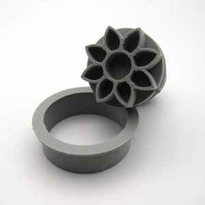 May include: A gray plastic cookie cutter in the shape of a flower with eight petals. The cutter is designed to create a decorative edge on cookies.