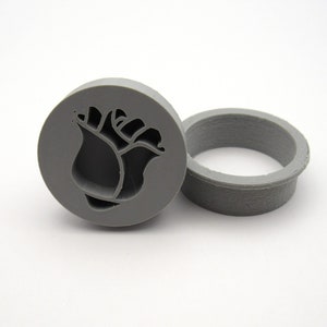 Puede incluir: Un molde de silicona gris con un diseño de rosa. El molde es redondo y tiene un borde elevado. Se utiliza para hacer fondant u otras decoraciones comestibles.