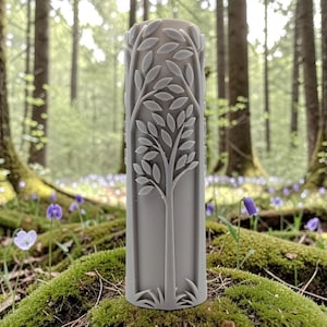 May include: A gray, cylindrical object with a detailed tree design. The tree features leaves and branches, and the object is set against a backdrop of a forest with moss and wildflowers.
