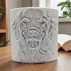 Pode incluir: Um recipiente cilíndrico branco com um relevo esculpido detalhado do rosto de um golden retriever na parte frontal. As características do cão, incluindo a textura do pelo, olhos, nariz e boca aberta, são apresentadas em acabamento branco.