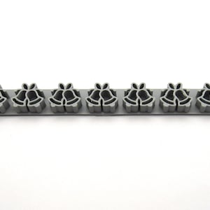 Puede incluir: Un borde de plástico gris con un patrón repetido de dos campanas. Las campanas están delineadas en un gris más oscuro.