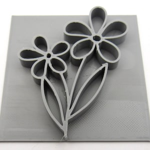 May include: A gray 3D printed square with a design of two stylized flowers with stems and leaves.