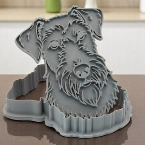 May include: A gray plastic cookie cutter in the shape of a dog's head. The cutter features detailed facial features, including eyes, nose, and fur texture. The cutter is designed to cut out dog-shaped cookies or other treats.