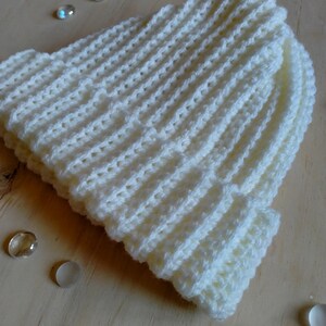 Puede incluir: Gorro de punto blanco con textura de canal&eacute;. El gorro est&aacute; sobre una superficie de madera clara.