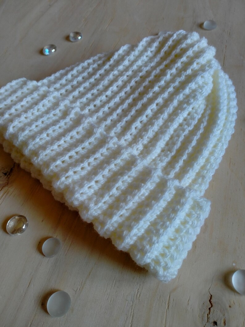 Puede incluir: Gorro de punto blanco con textura de canal&eacute;. El gorro est&aacute; sobre una superficie de madera clara.